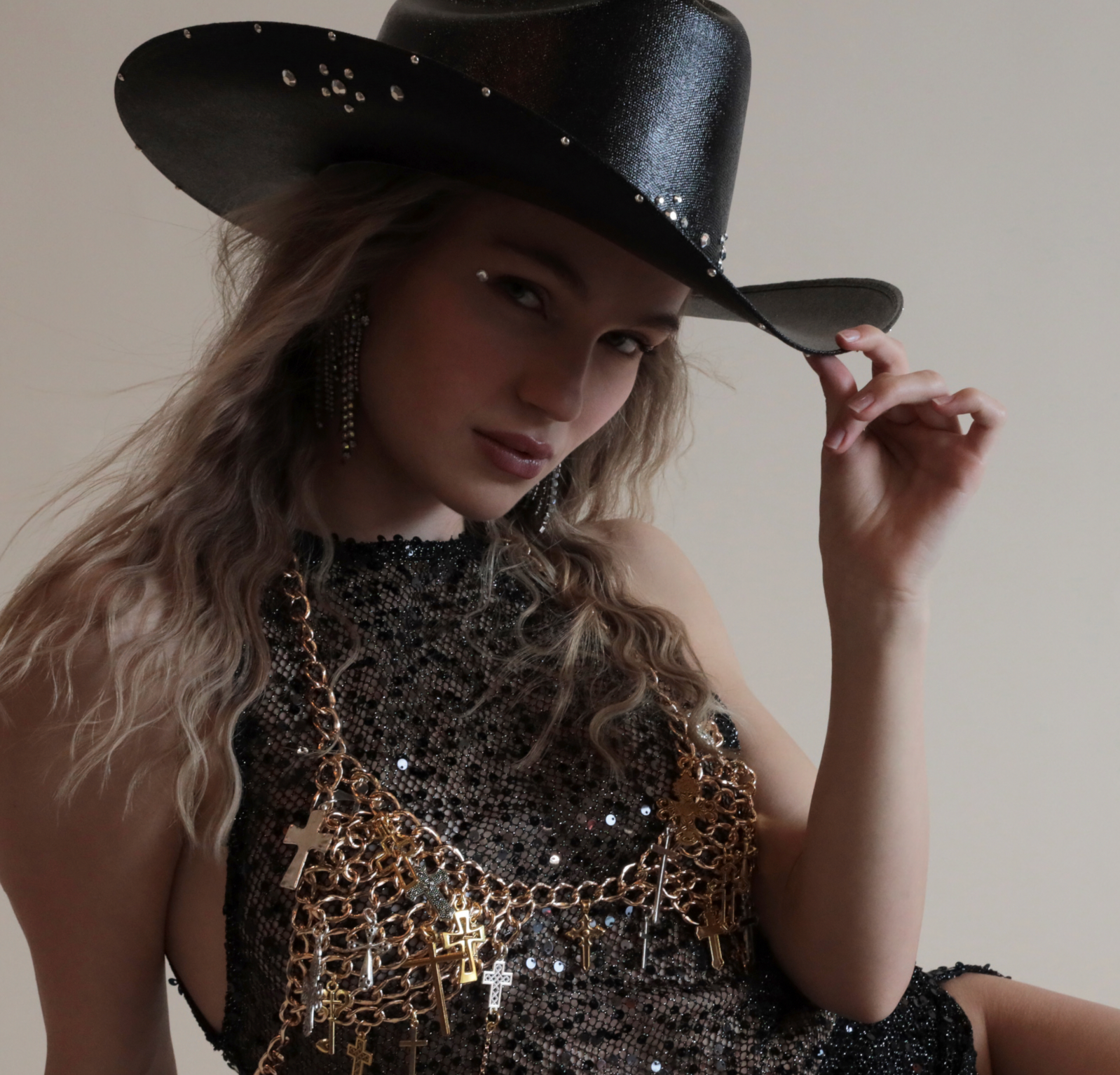 Black cowboy hat with metallic jewels paired with gold chain bra and black sequin dress.