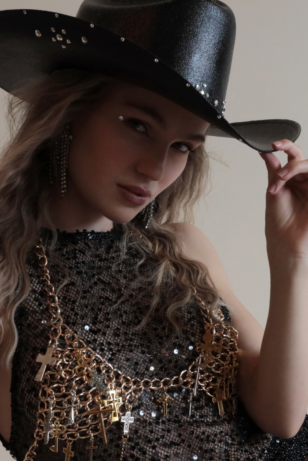 Black cowboy hat with metallic jewels paired with gold chain bra and black sequin dress.