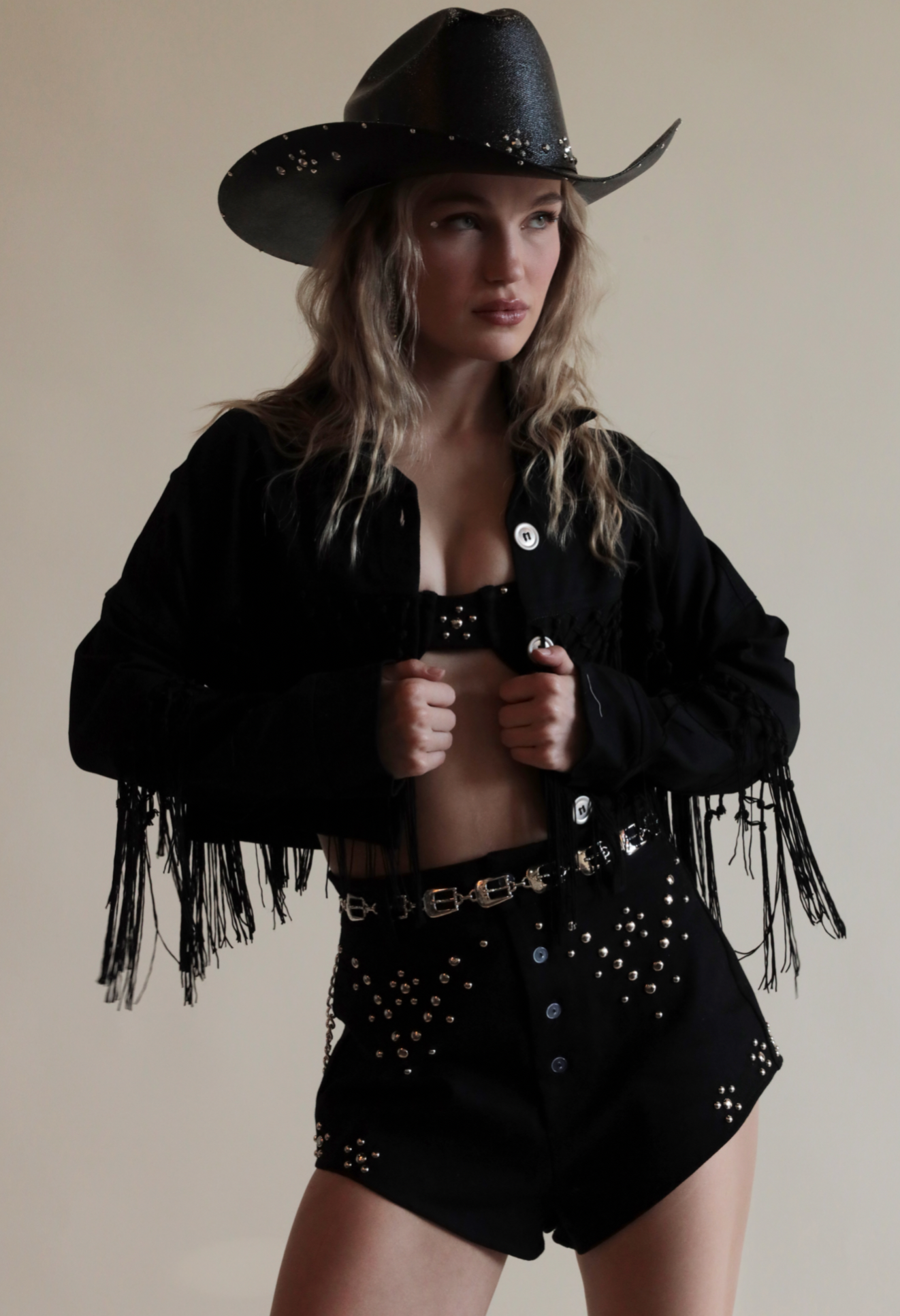 Black cowboy hat with metallic jewels paired with denim grommeted set and fringe jacket.